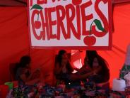 Children sitting in a red stand with bags of cherries for sale with a sign above that reads "Flathead Cherries"
