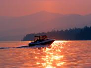 a boat creating wake on a calm Flathead Lake as the sun sets in the backgorund