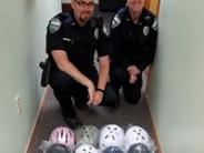 2 Police officers kneeling next to new bicycle helmets for the local youth