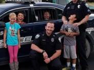 Police officers making funny faces in front of their police vehicle with multiple children 