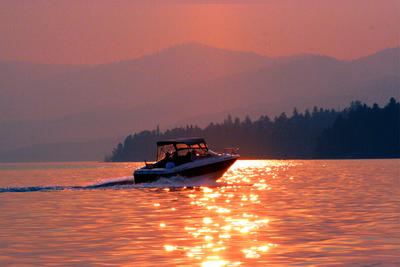a boat creating wake on a calm Flathead Lake as the sun sets in the backgorund