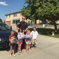 4 children posing with a police officer in front of a police car holding their new bicycle helmets