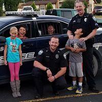 Police officers making funny faces in front of their police vehicle with multiple children 