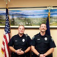 two police officers stand in between the U.S. flag and the Montana flag at the City Commission chambers